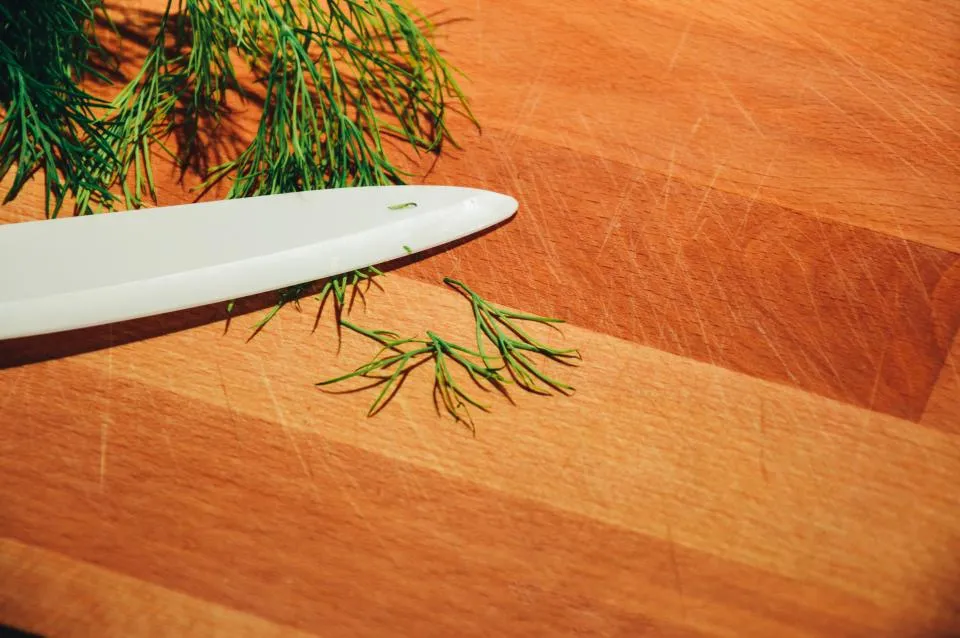 Knife blade on a wooden cutting board with fresh dill